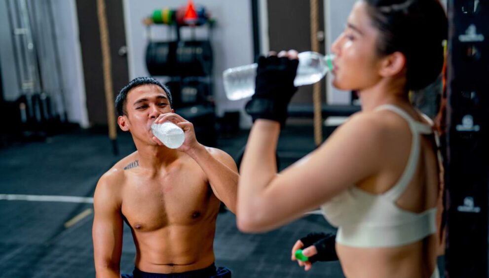 Asian sport man and woman drink water from bottle after finish of training in fitness gymm.