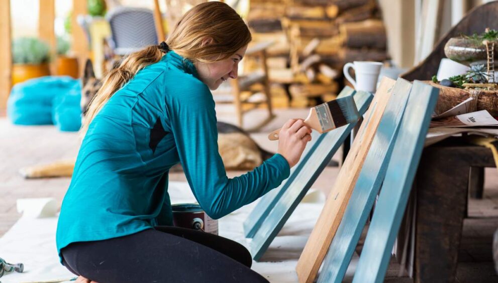 Teenage girl painting wooden shelves blue.