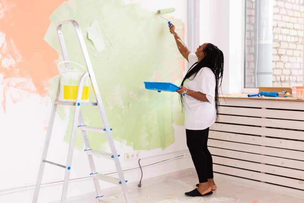 Beautiful african american girl painting the wall with paint roller. Portrait of a young beautiful woman painting wall in her new apartment. Redecoration and renovation concept