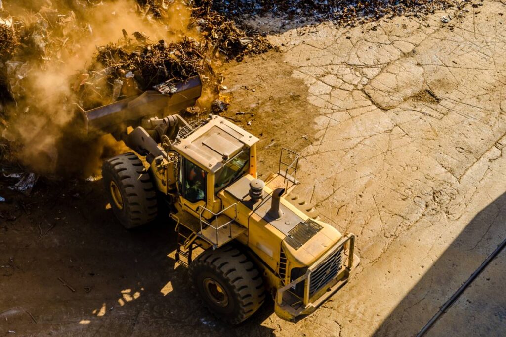 A horizontal shot of a yellow front loader tractor carrying dusty waste, caterpillar exhausts part