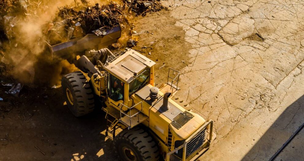 A horizontal shot of a yellow front loader tractor carrying dusty waste, caterpillar exhausts part