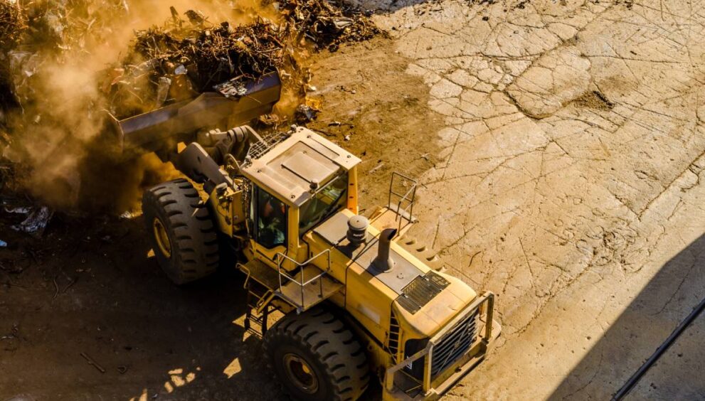 A horizontal shot of a yellow front loader tractor carrying dusty waste, caterpillar exhausts part