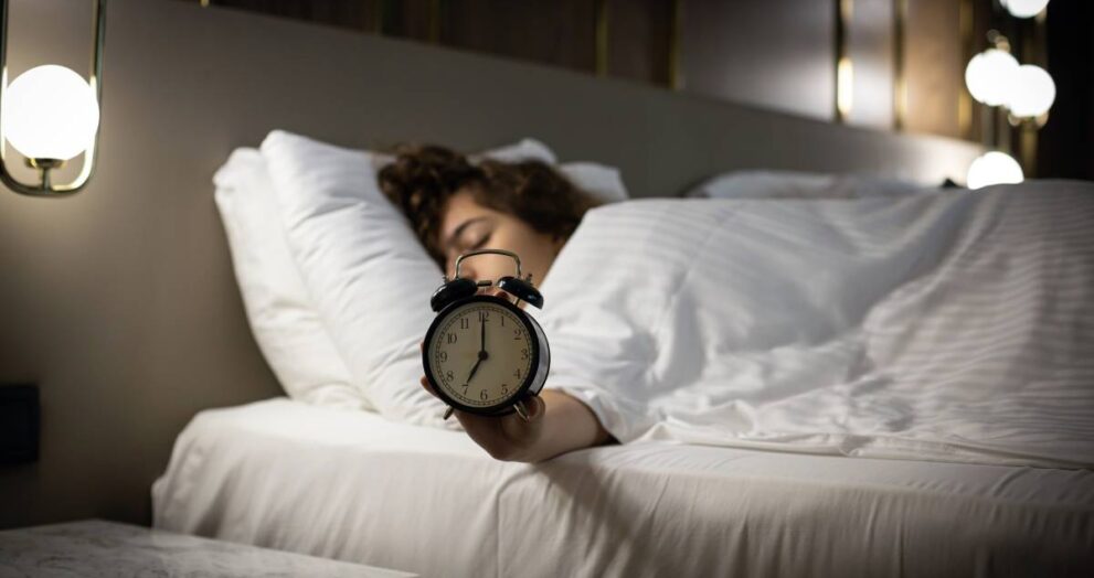 alarm-clock-on-the-bed-with-sleeping-woman-behind-2024-10-17-01-48-49-utc (1)