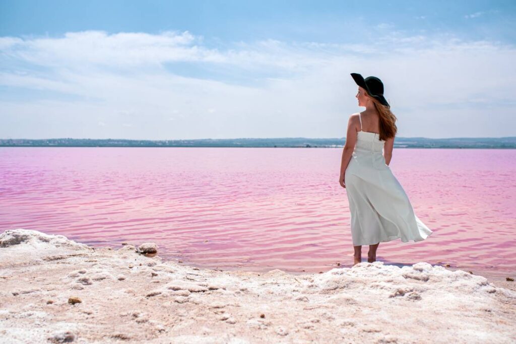 Back view of cute teenager woman wearing white dress walking on a amazing pink lake