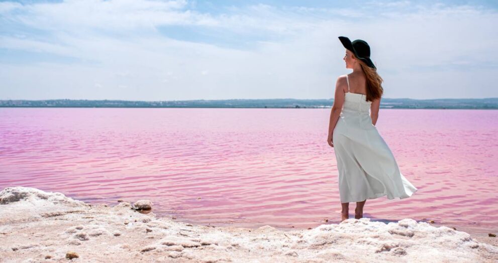 Back view of cute teenager woman wearing white dress walking on a amazing pink lake