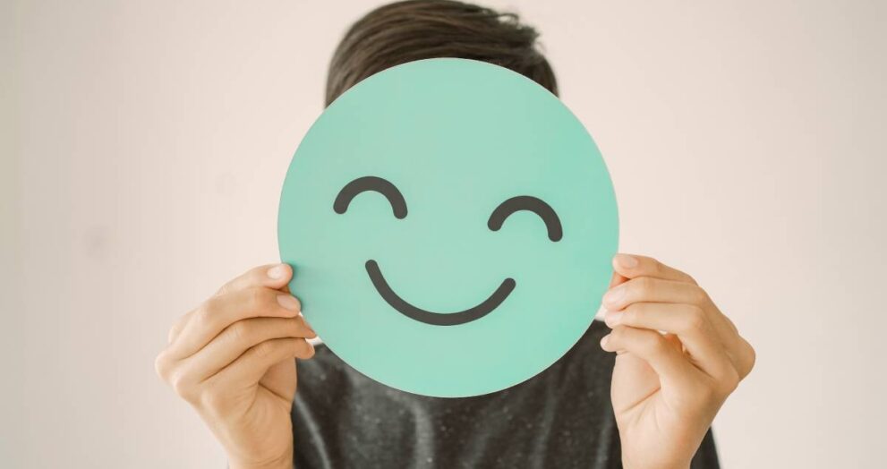Happy mixed Asian teen boy holding smile emoji face, positive mental health concept