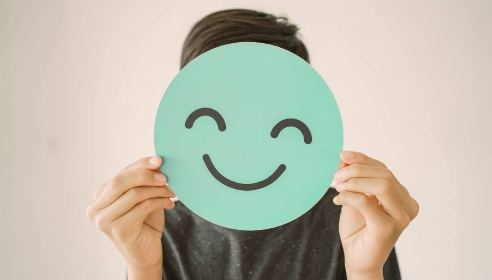 Happy mixed Asian teen boy holding smile emoji face, positive mental health concept