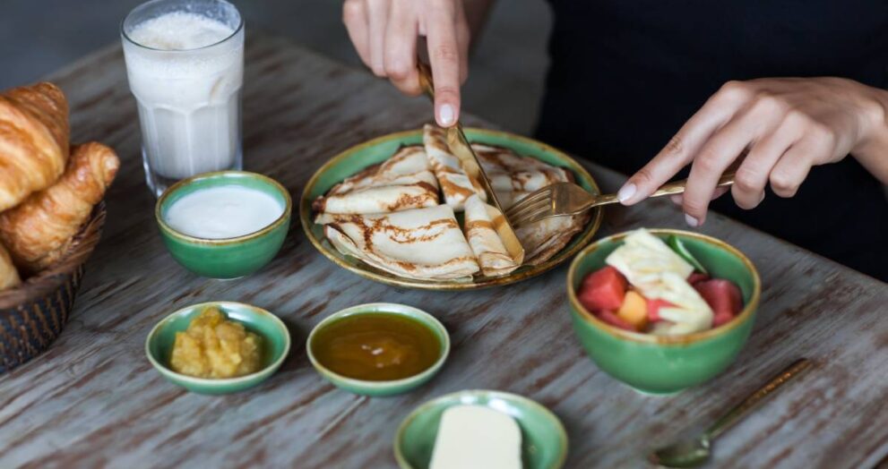Young woman having breakfast and cut pankaces with golden fork and knife