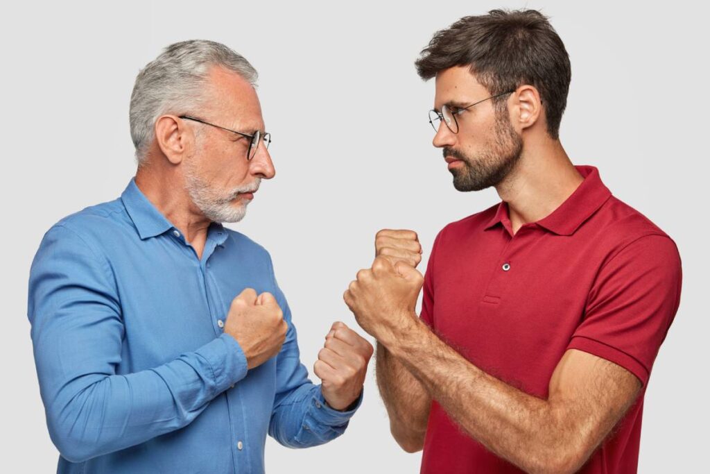 Sideways shot of two men competitors look seriously at each other, keeps hand clenched in fists, ready to fight, can`t share common business, stand against white background. People and competition